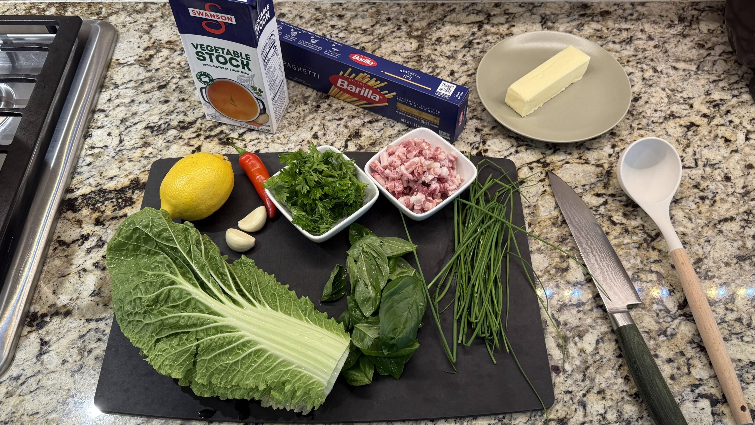 Fresh ingredients for garlic herb butter pasta including garlic, herbs, lemon, pancetta, and pasta on a cutting board