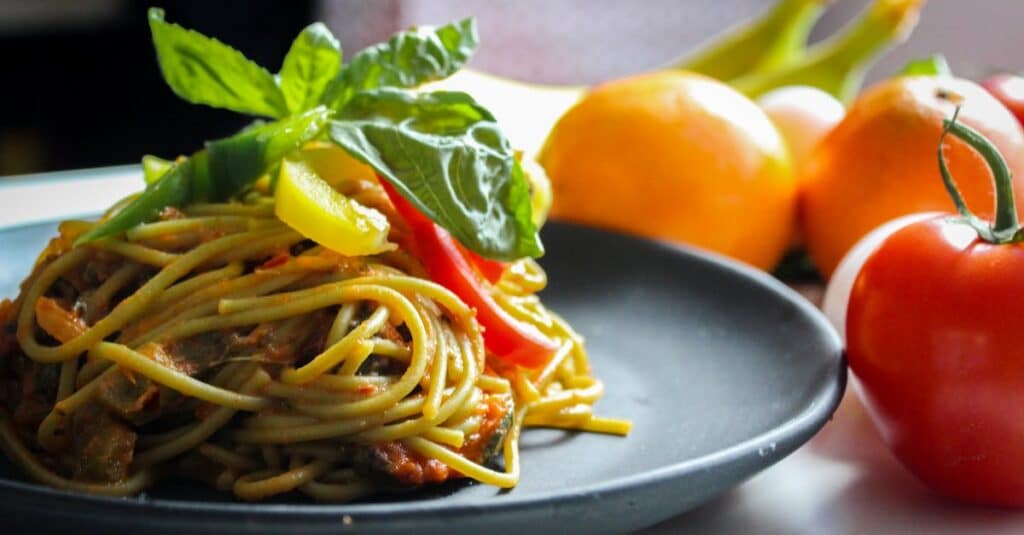 A plate of spaghetti garnished with basil and fresh vegetables, showcasing Italian cuisine.